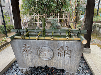 The purification font, with a system of bamboo pipes set on top of it. Water flows out past the front of the font.