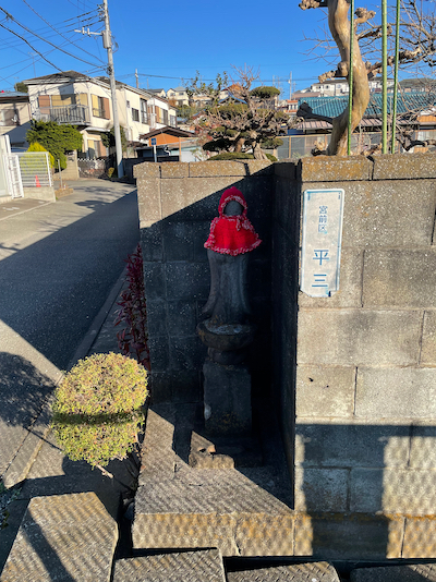 A small stone Jizō statue, wearing a knitted red hat and bib.