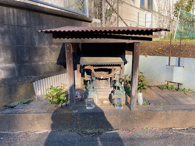 A very small Inari shrine, with green foxes and a simple roof.